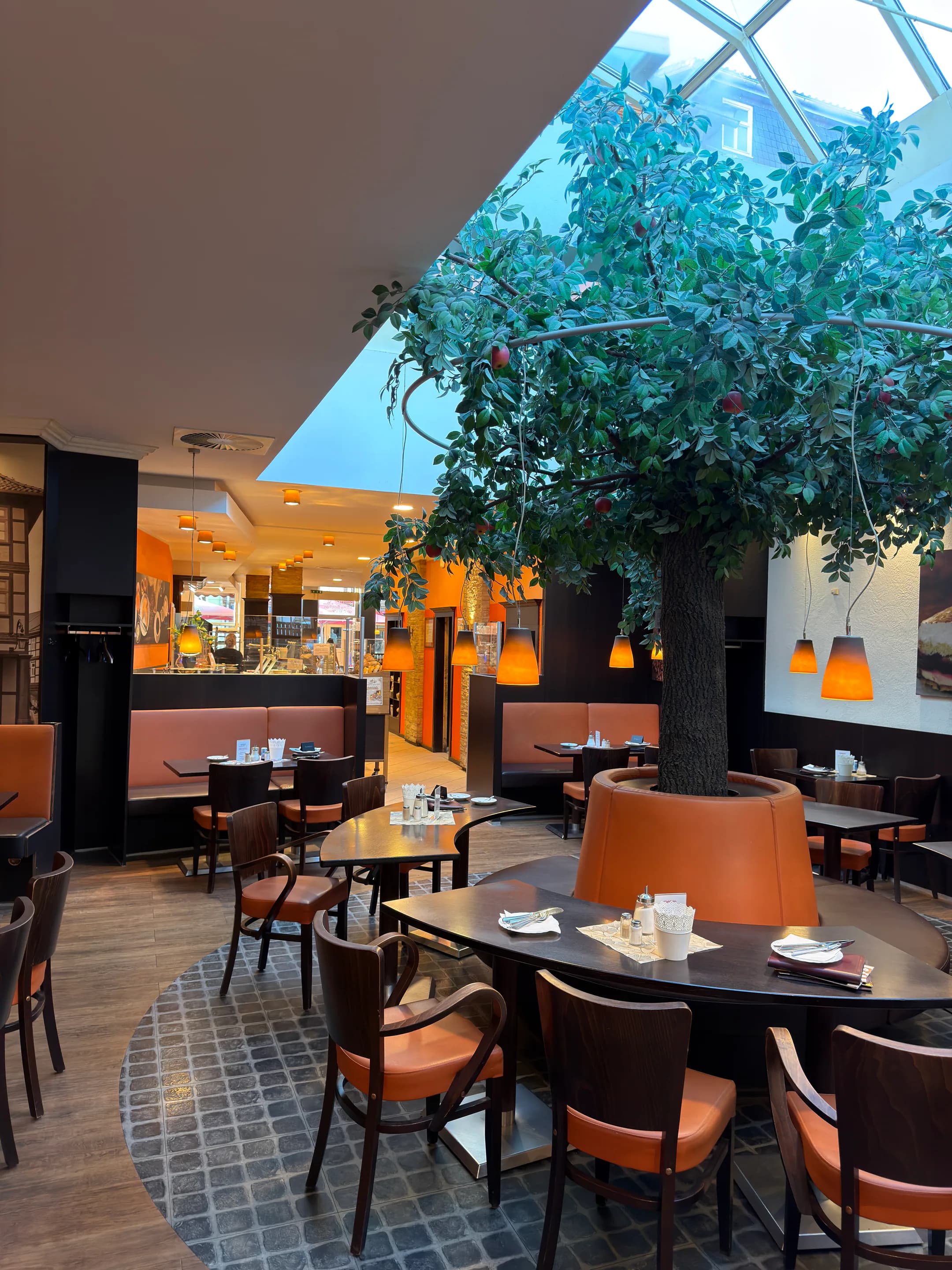 Gastraum des Schlemmercafés in Wernigerode mit großem Baum, Sitzecken und orangefarbenen Pendelleuchten
