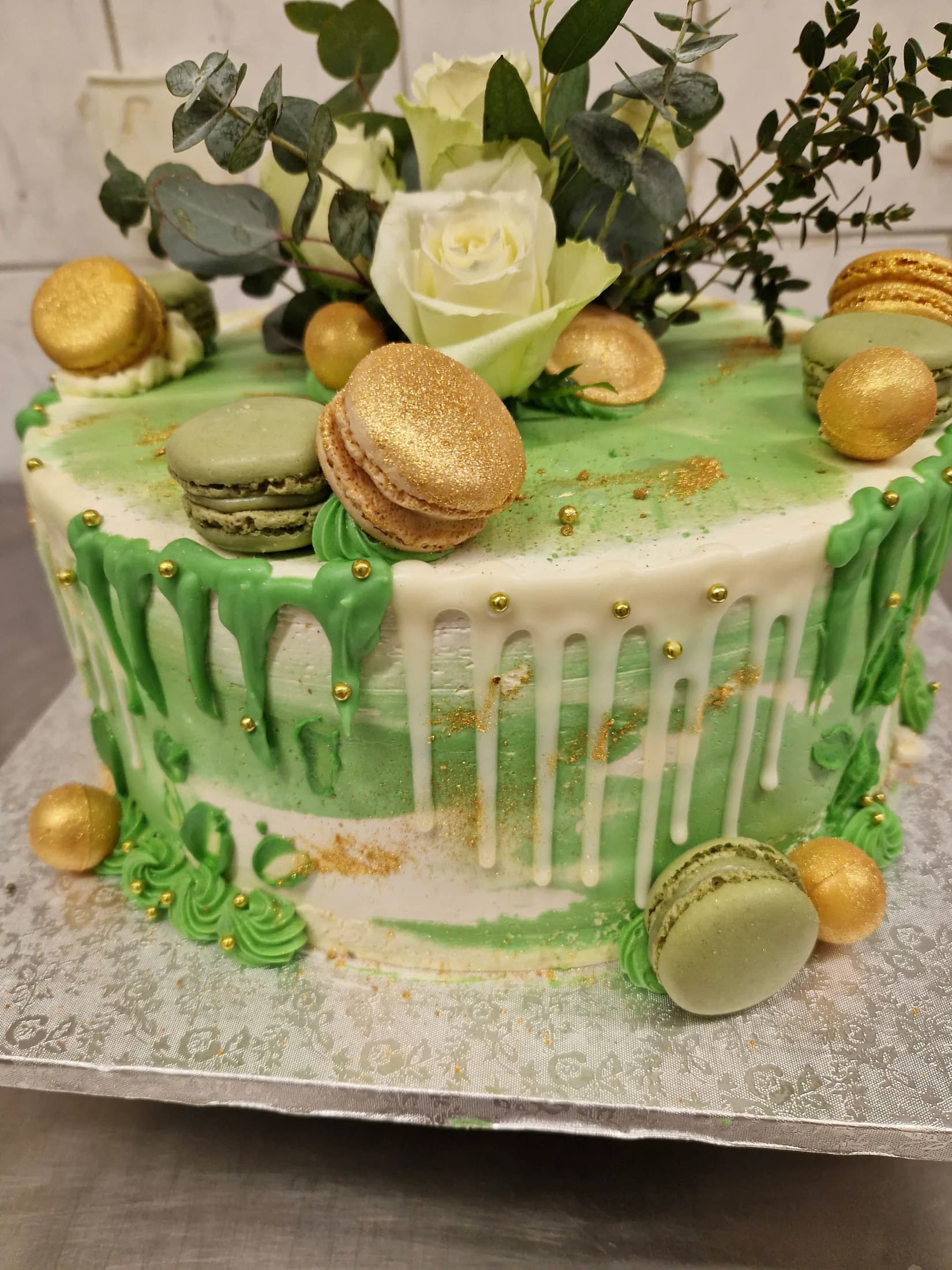 Grün-weiße Festtagstorte mit goldenen Macarons, Rosen und Eukalyptus aus der Konditorei des Schlemmercafés