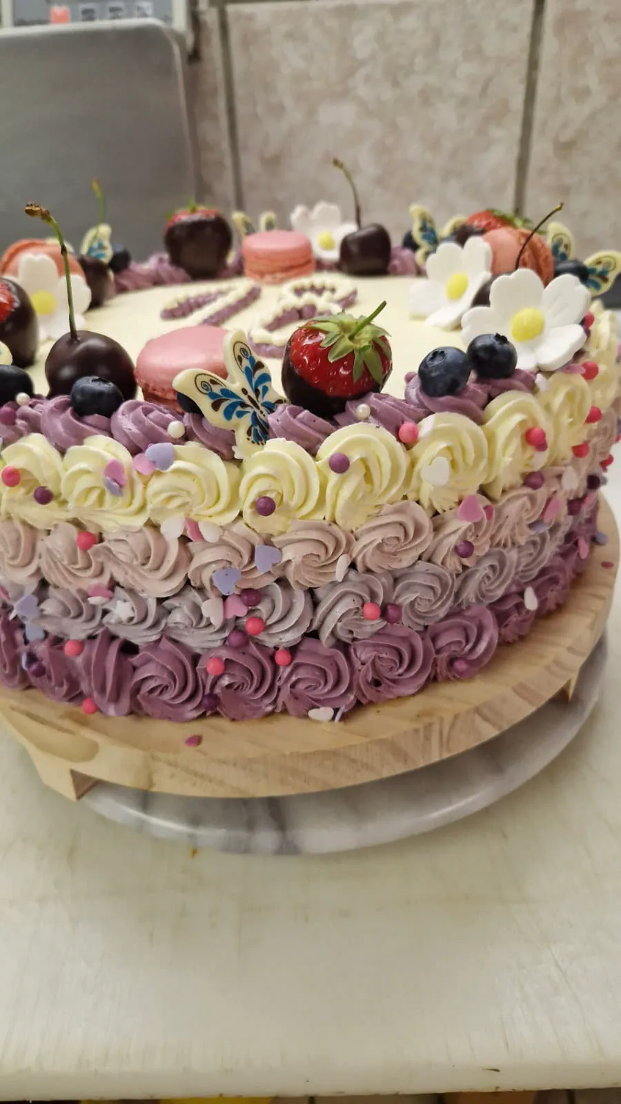 Festliche Torte mit violetten Cremetupfen, Früchten, Macarons und Schmetterlingen