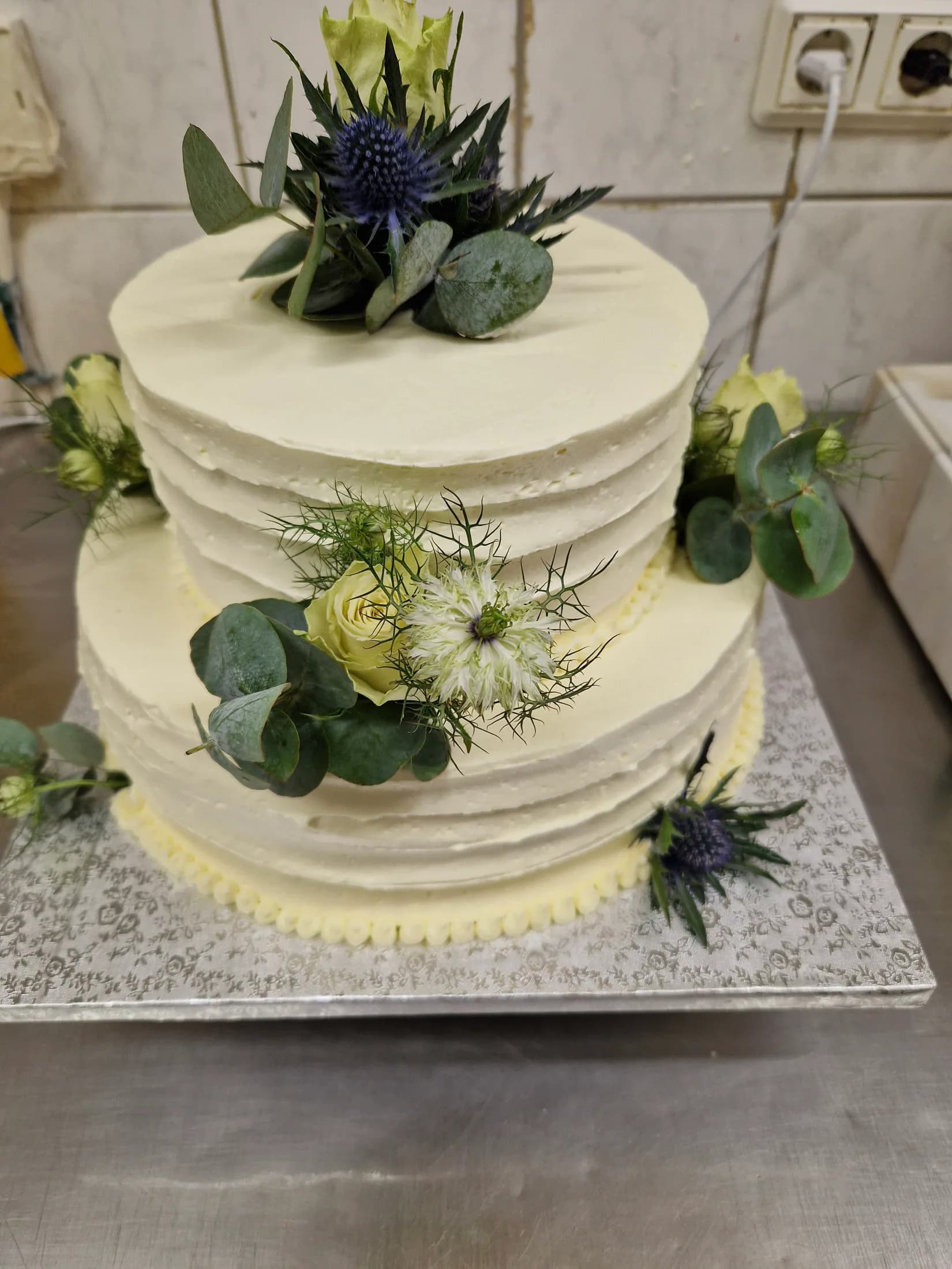 Zweistöckige Hochzeitstorte mit weißen Blüten, Disteln und Eukalyptus aus der Konditorei des Schlemmercafés